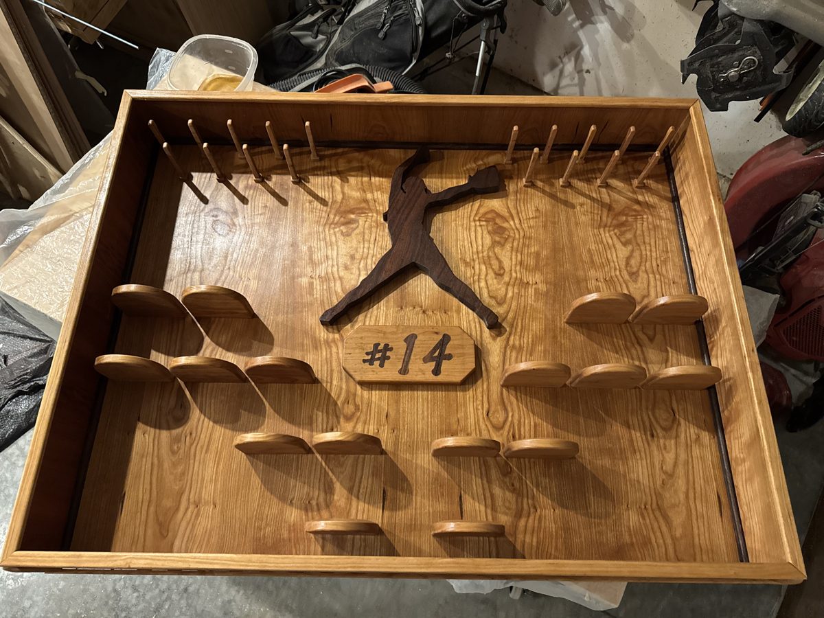 Trophy case after staining showing peg holders, pitcher silhouette inlay, and #14 plaque